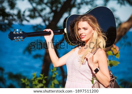 Blonde woman having acoustic guitar. Female playing music on seaside