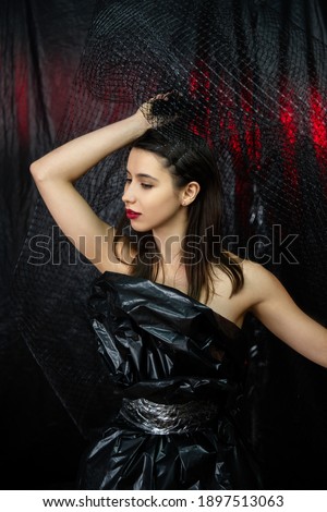 Fashion portrait. Beauty care. Aesthetic cosmetology. Relaxed model woman with perfect face skin red lips posing in black polyethylene dress isolated on dark night background.