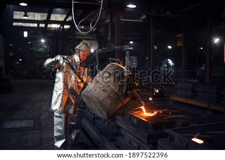 Iron casting in smelter factory. Foundry worker pouring liquid steel into molds. Royalty-Free Stock Photo #1897522396