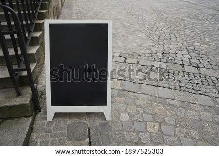 empty blank of  black chalkboard.  The board stands on an empty street pavement with copy space. Stoned stairs with iron railings. Linz, Germany.