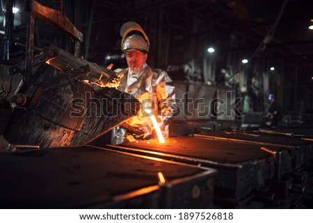 Foundry workman pouring molten iron into molds for steel production. Heavy industry and metallurgy process. Royalty-Free Stock Photo #1897526818