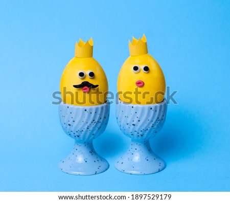 Cute Easter greeting card on a blue background. King and queen eggs. Yellow eggs with faces made from plasticine and paper crown. 