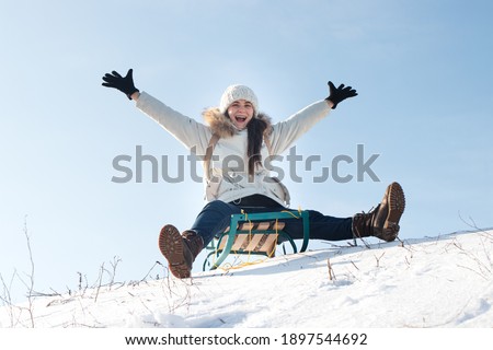 Woman sits and sledges from the mountain against the background of snow and sky in winterGirl laughs and rejoices in snow, entertainment in the sled.