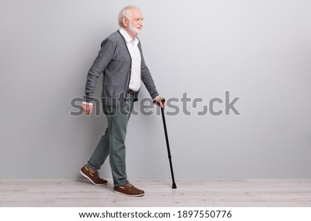 Full size profile photo of old man go with wand wear dark sweater trousers isolated on grey wall Royalty-Free Stock Photo #1897550776