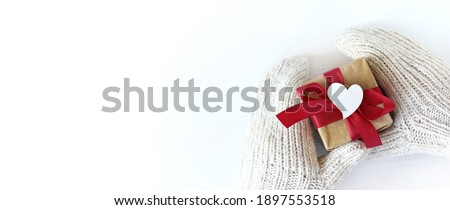 hands in mittens with a gift and a heart symbol. receiving or giving on the holiday of lovers
