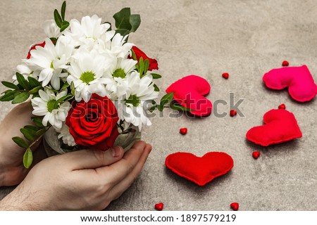 Valentine's Day or Happy Birthday concept. Male hands are holding a bouquet of flowers. Scattered handmade felt hearts, grey stone concrete background, copy space