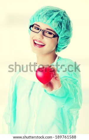 Smiling female doctor or nurse in surgical clothes holding red heart 