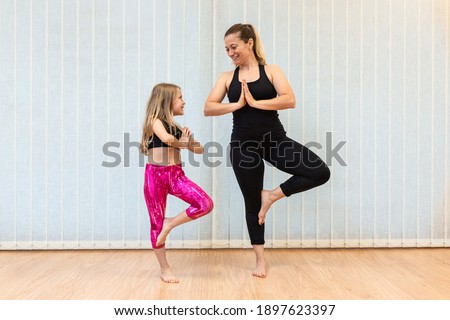 the mother yoga instructor and the daughter perform the tree position