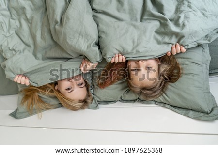 Woman with little girl hides under blanket. Morning, mother and daughter have a fun. Focus on girls eyes.