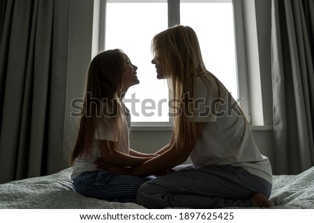 Mom with little girl in bed, silhouette. Window on background.