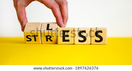 Having less stress or being stress-less. The word 'STRESS' and 'LESS' on wooden cubes. Male hand. Beautiful yellow table, white background, copy space. Business and psychological less stress concept.