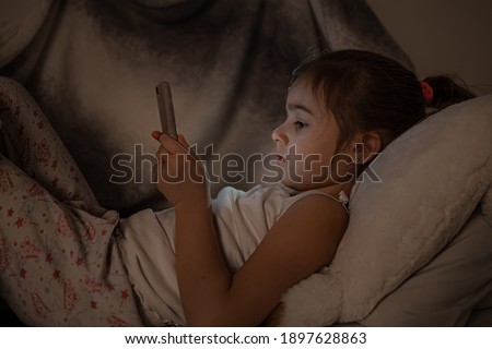 Little girl watching smartphone in bed, kid using phone and play game, child using mobile, addicted game and cartoon.