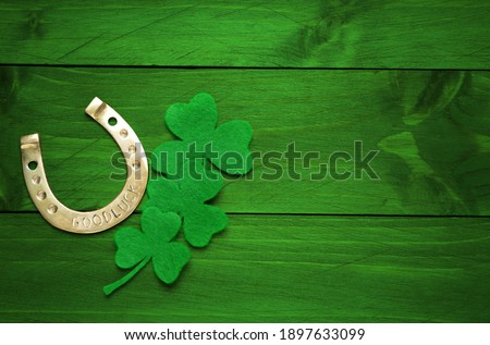 Decorative clover leaves and horseshoe on green wooden background, flat lay with space for text. St. Patrick's Day celebration