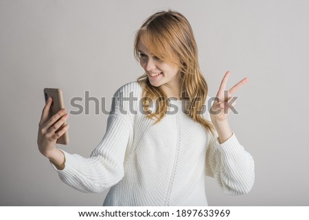 Beautiful young girl on a white background in the studio makes a selfie on a smartphone
