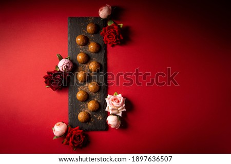 Chocolates lie on a slate on a red table surface. Festive table setting. Dessert serving. Romance. A romantic dessert for the holiday. Sweet gift.