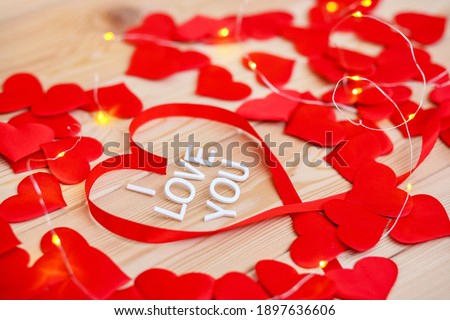 White letters congratulations on Valentine's Day.Happy holiday of lovers men and women.Top view of many beautiful red hearts made of ribbon on wooden background.I love you.February 14 in winter