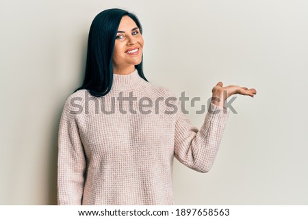 Young caucasian woman wearing casual winter sweater smiling cheerful presenting and pointing with palm of hand looking at the camera. 