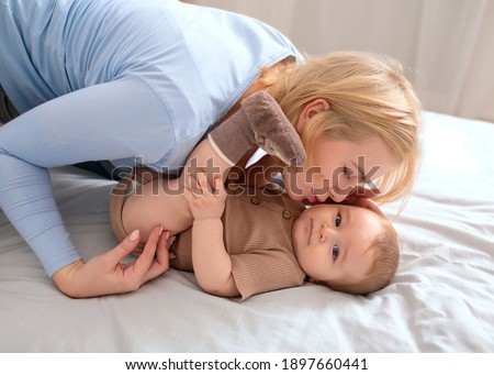 Mother and kid, family concept. Loving caucasian mother kissing her beautiful little baby at home, laying together on bed. Blonde woman bonding with her cute kid toddler, closeup