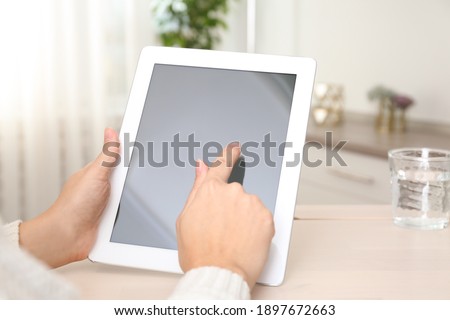 Woman using tablet at table indoors, closeup
