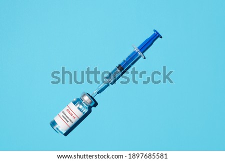 Covid-19 vaccine and syringe close-up, flat lay on a blue background. Vaccination concept