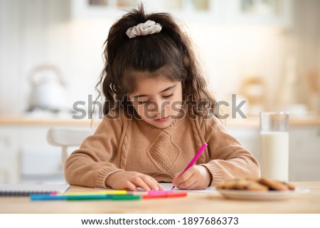Adorable Little Girl Drawing Picture At Home, Sitting At Table In Kitchen Using Colorful Markers. Cute Female Kid Having Fun At Home, Enjoying Development Activities, Closeup Shot With Free Space
