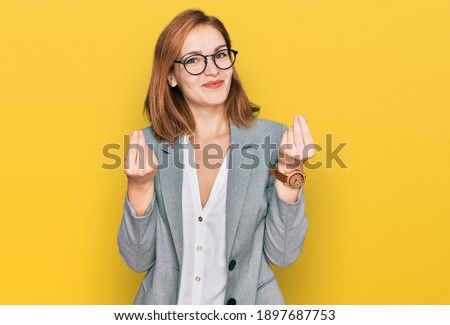 Young caucasian woman wearing business style and glasses doing money gesture with hands, asking for salary payment, millionaire business 