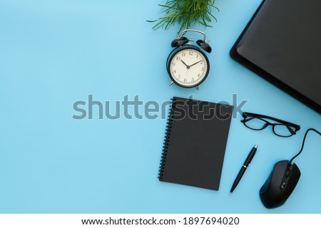 Creative flat lay design of workspace desk with laptop, alarm clock, blank notebook, stationery with blue copy space background.