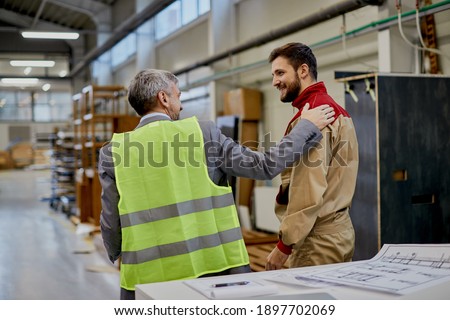 Happy factory worker communicating with company manager at woodworking industrial facility.  Royalty-Free Stock Photo #1897702069