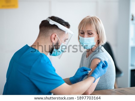 Coronavirus prevention and treatment concept. Senior female patient getting vaccinated against covid-19 at clinic. Young medic making antiviral vaccine injection to mature woman Royalty-Free Stock Photo #1897703164
