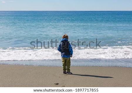 Beautiful little boy looking into the sea. Winter sea on ligurian coast in Riva Trigoso, Genova, Italy