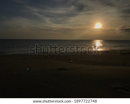 A photograph of a cloudless sky, a clear sun, calm waves, and a beautiful afternoon beach with cool air