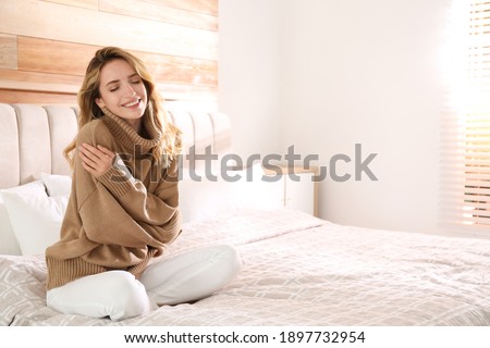 Beautiful young woman wearing warm brown sweater on bed at home. Space for text Royalty-Free Stock Photo #1897732954