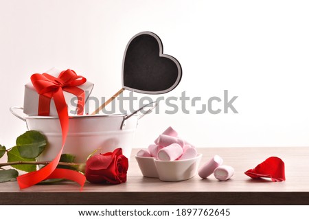 Romantic celebration with gift, rose, and container with jelly and sugar sweets on wooden table with white isolated background. Front view.