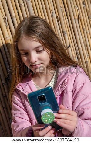 teenage girl in a purple jacket taking pictures of herself (selfie) or looking at her smartphone