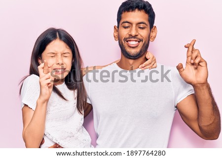 Young father and daughter wearing casual clothes gesturing finger crossed smiling with hope and eyes closed. luck and superstitious concept. 