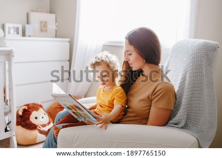 Mom reading book with baby boy toddler at home. Early age children education development. Mother and child kid spending time together. Family authentic candid lifestyle. 