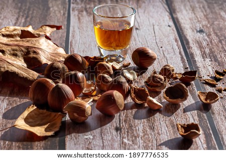 Hazelnuts and hazelnut shells in a bamboo bowl with a glass of sweet wine on wooden surface.