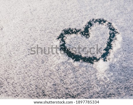 Love symbol in snow on window. Valentine's day sign on car. Free copy space for text.
Heart shape in snow drawn by hand on snowy car window at evening light. 