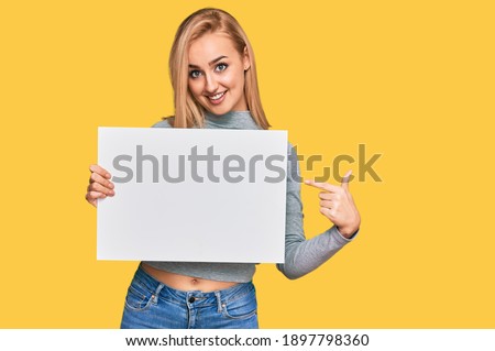 Beautiful caucasian woman holding blank empty banner smiling happy pointing with hand and finger 