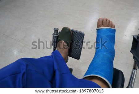 Focus on the blue splint on the right leg of an Asian woman sitting in a wheelchair.