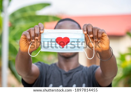 close up image of surgical mask, with a symbol of love, black hand with face mask