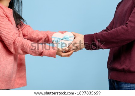 Close up beautiful couple in love on blue studio background. Saint Valentine's Day, love, relationship and human emotions concept. Copyspace. Young man and woman holding one heart box with gift or