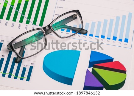 Black rimmed glasses and analytical charts on the desktop. Stock market analysis. Earnings and success. Business concept. Presentation background.