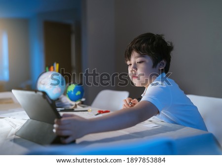 New normal life kid using tablet for his homework in cinematic tone, Child boy doing homework by using digital tablet searching information on internet,E-learning, Home schooling education concept