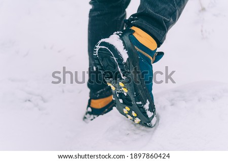 The man has ice shoes on his shoes. A people walks in the snow in winter