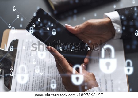 A businesswoman in formal wear checking the phone to sign the contract to prevent probability of risks in cyber security. Padlock Hologram icons over the working desk.