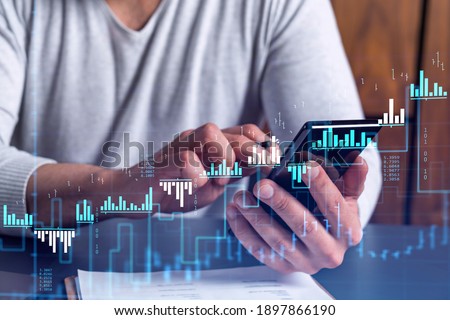 Trader holding in the hands a smart phone and researching stock market to proceed right investment solutions. Internet trading and wealth management concept. Hologram Forex chart over close up shot.