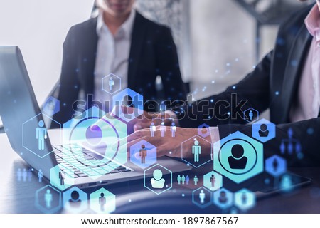 Two HR specialists in formal wear analyzing the recruitment market using laptop to boost the intern program at international consulting company. Social networking hologram icons. Royalty-Free Stock Photo #1897867567