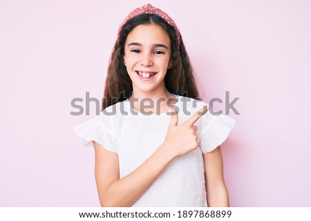 Cute hispanic child girl wearing casual clothes and diadem cheerful with a smile of face pointing with hand and finger up to the side with happy and natural expression on face 