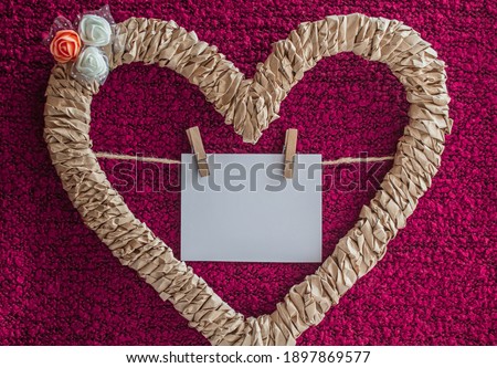 Braided heart decorated with flowers with a card on a thread on a pink background